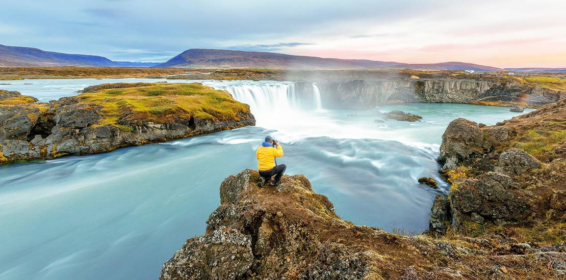 A man taking a photograph of Godafoss waterfall in Iceland